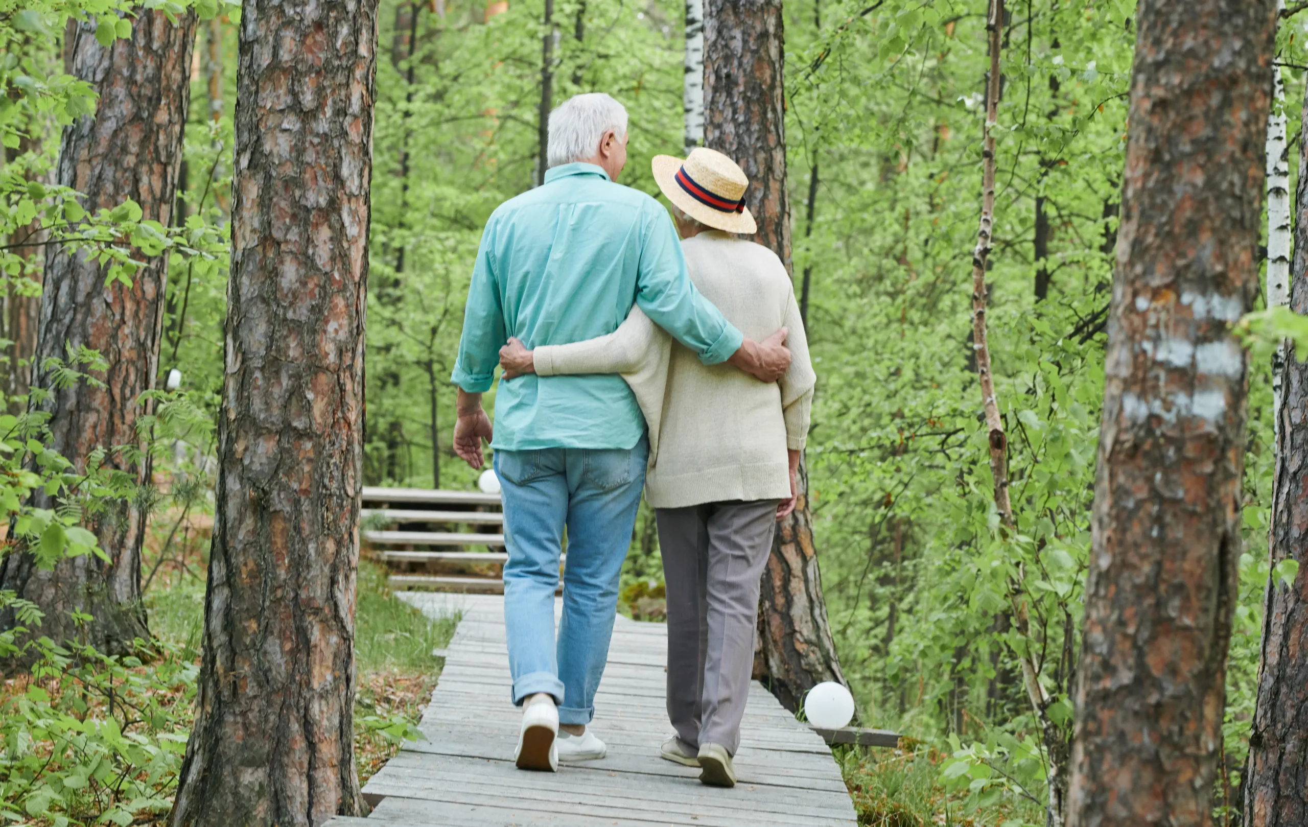 Rear view of affectionate senior couple taking a walk in the forest on a summer day